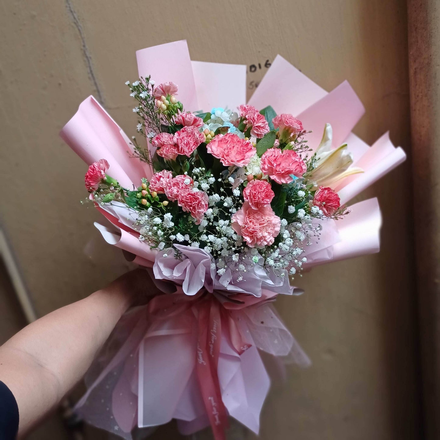 Bouquet of pink flowers wrapped in pink paper held by a person.