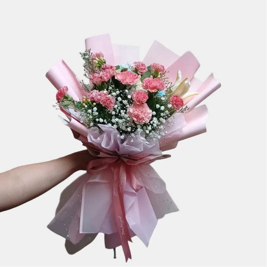 Bouquet of pink flowers with ribbons held by a person against a plain background