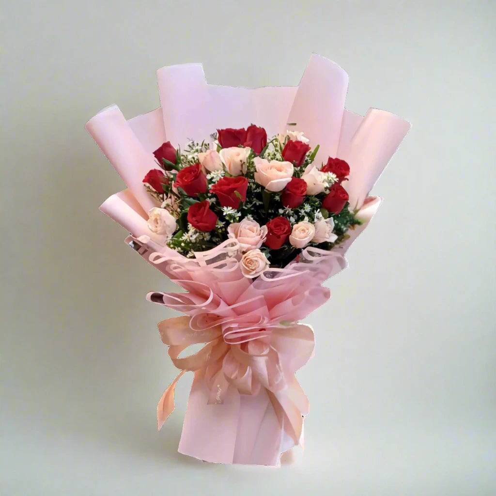 Bouquet of red and pink roses wrapped in pink paper with a bow on a light gray background
