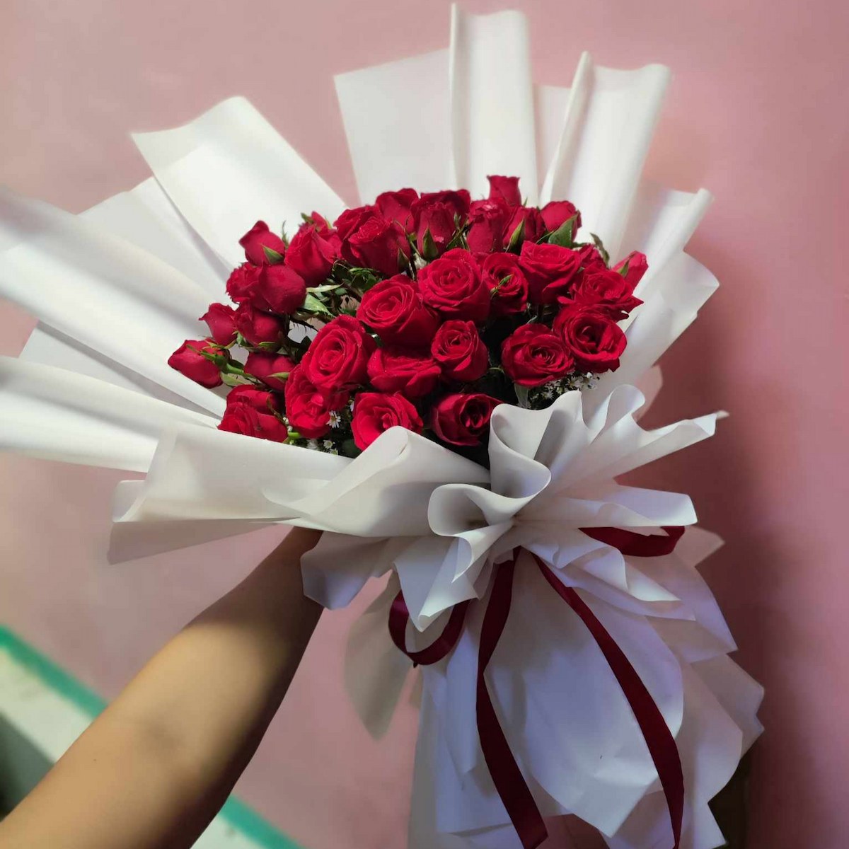 Bouquet of red flowers with white paper and ribbons against a pink background