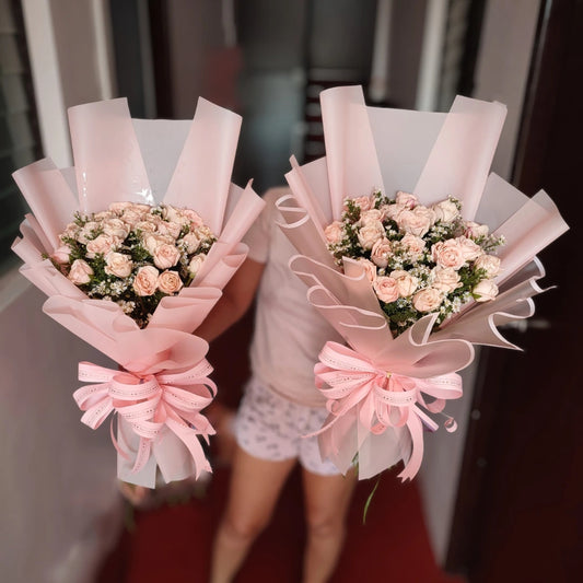 Two bouquets of flowers wrapped in pink paper with ribbons held by a person.