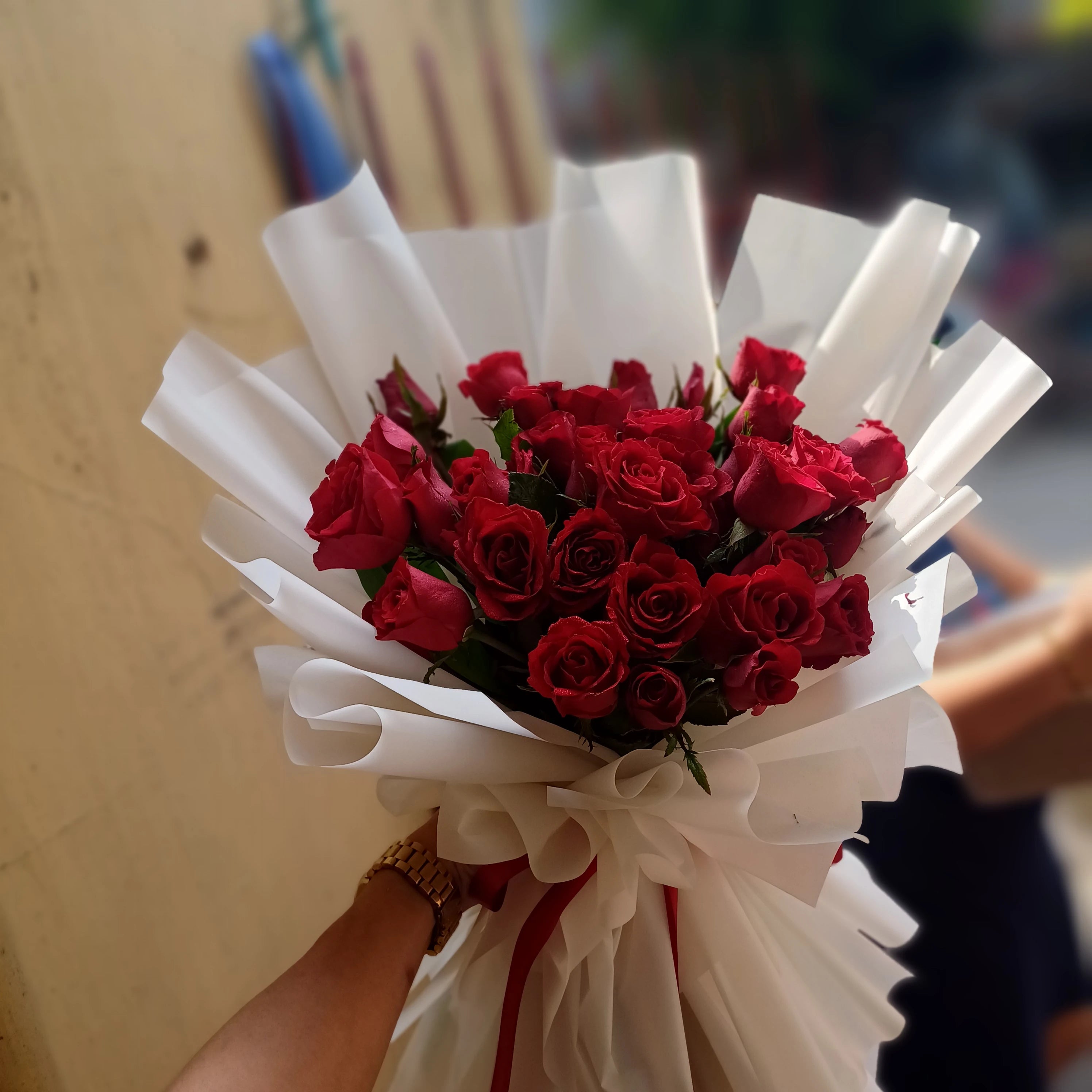 Bouquet of red roses wrapped in white paper held by a person.