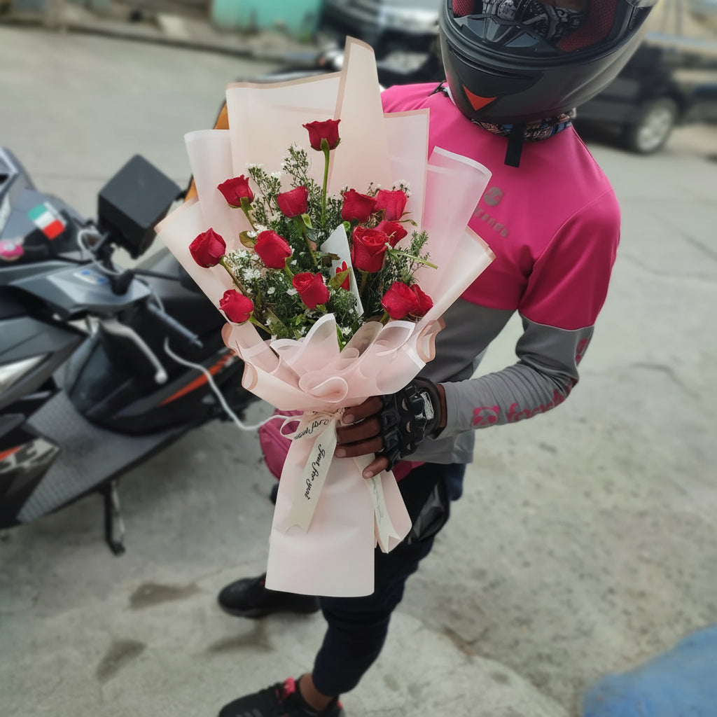 Person in pink and gray jacket holding a bouquet of red roses, with a motorcycle in the background.