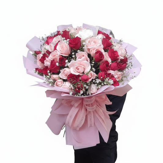Bouquet of red and pink roses with a pink ribbon held by a person against a neutral background.