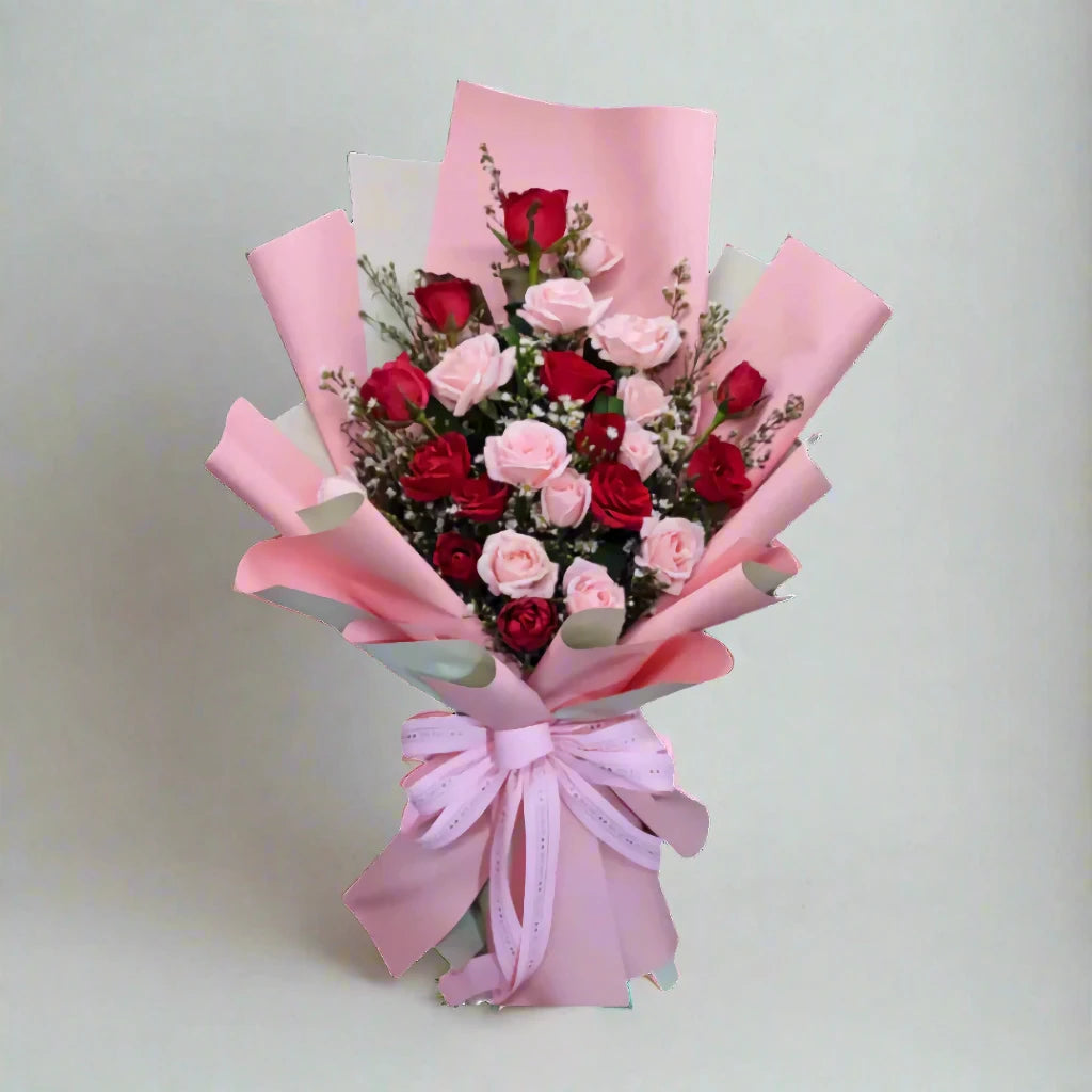 Bouquet of red and pink roses wrapped in pink paper with a bow on a light gray background