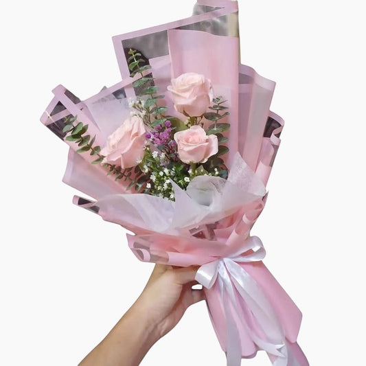 The Flowercart Rosa bouquet featuring three pink roses, eucalyptus, and gypsophila wrapped in pink paper with a ribbon.