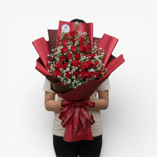 The Flowercart Valley Scent bouquet: 24 red roses with baby's breath, wrapped in red and burgundy paper, tied with a red ribbon.