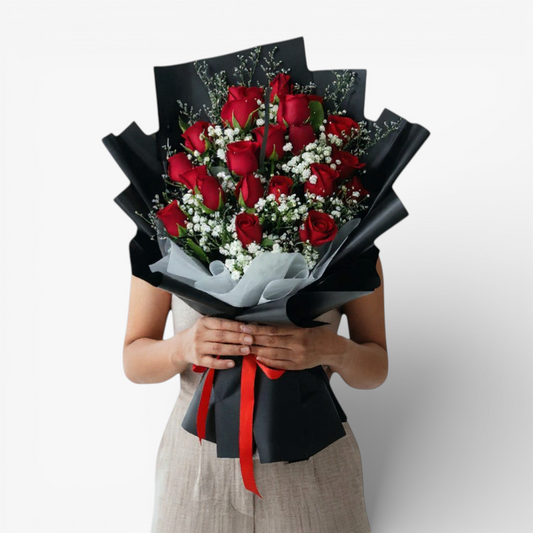 The Flowercart Luxe Noir bouquet: 24 red roses with white fillers, wrapped in black paper and tied with a red ribbon.