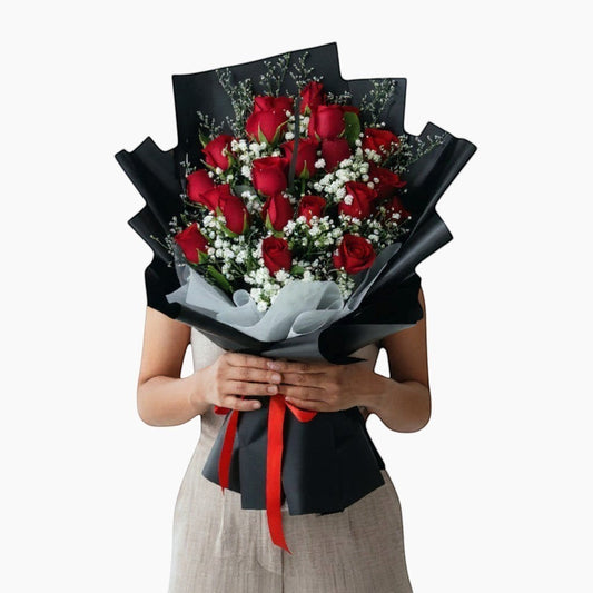 The Flowercart Luxe Noir bouquet: 24 red roses with white fillers, wrapped in black paper and tied with a red ribbon.