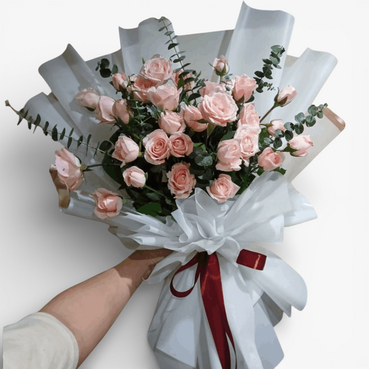 The Flowercart's Lovely Spark bouquet: 24 baby pink roses with eucalyptus, wrapped in white paper and tied with a burgundy ribbon.