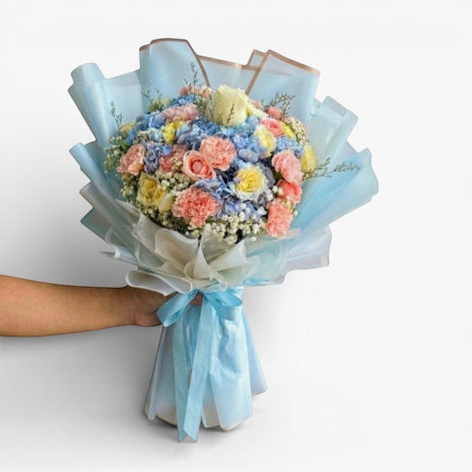 The Flowercart Pastel Blossom bouquet with pink roses, white roses, blue hydrangea, yellow roses, pink carnations, and baby's breath.