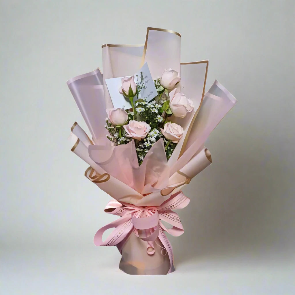 Bouquet of pink roses wrapped in pink paper with gold accents on a light gray background