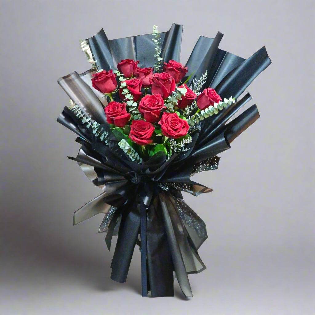 Bouquet of red roses wrapped in black paper with ribbons on a white background