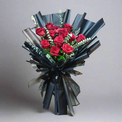 Bouquet of red roses wrapped in black paper with ribbons on a white background