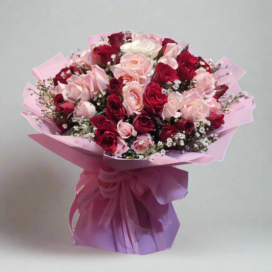 Bouquet of red, pink, and white roses wrapped in pink paper on a light gray background