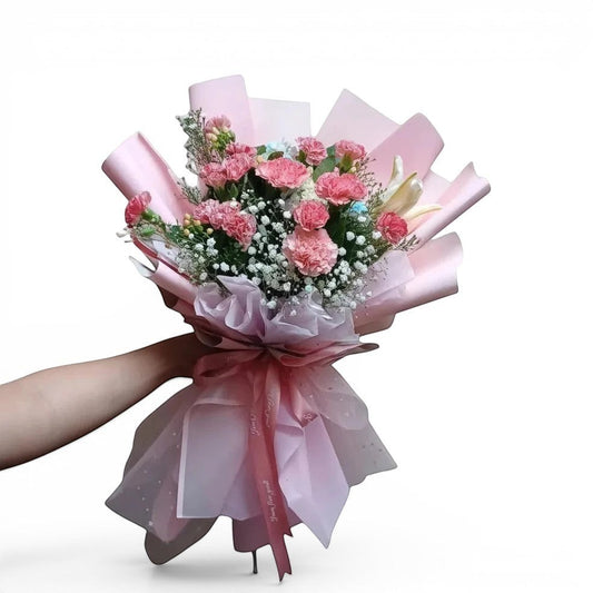Bouquet of pink flowers with ribbons held by a person against a plain background