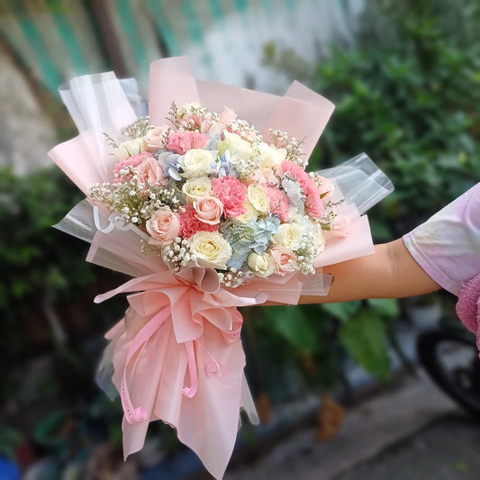 Bouquet of flowers wrapped in pink paper held by a person with a blurred green background