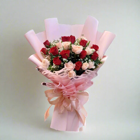 Bouquet of red and pink roses wrapped in pink paper with a bow on a light gray background