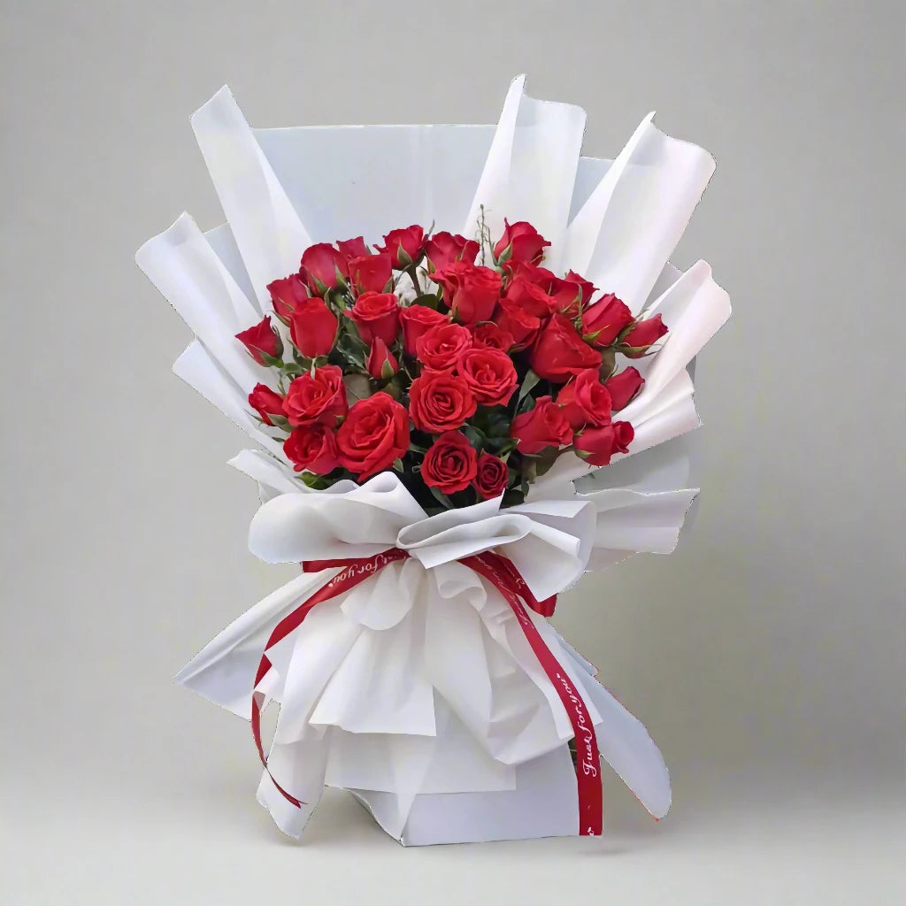 Bouquet of red roses wrapped in white paper with a red ribbon on a light gray background