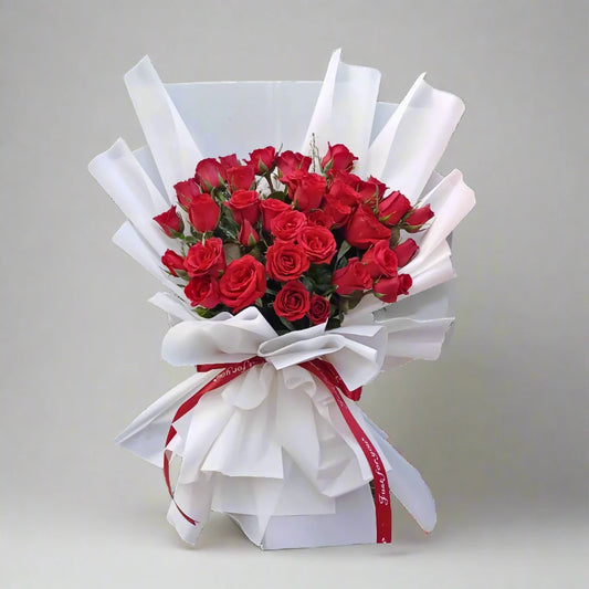 Bouquet of red roses wrapped in white paper with a red ribbon on a light gray background