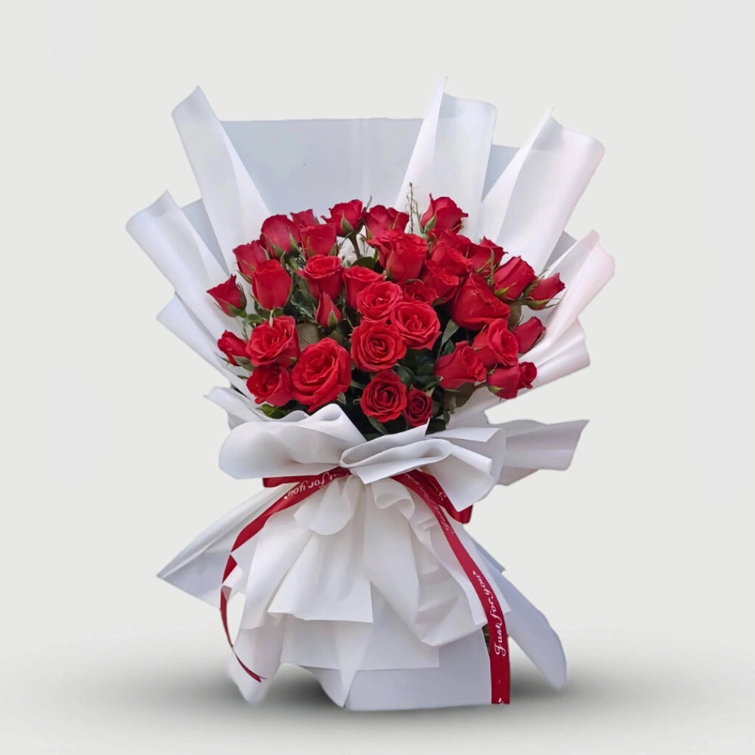 Bouquet of red roses wrapped in white paper with a red ribbon on a light gray background