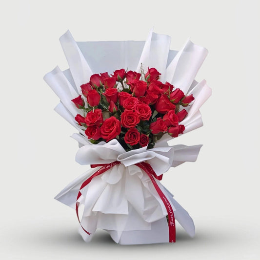 Bouquet of red roses wrapped in white paper with a red ribbon on a light gray background