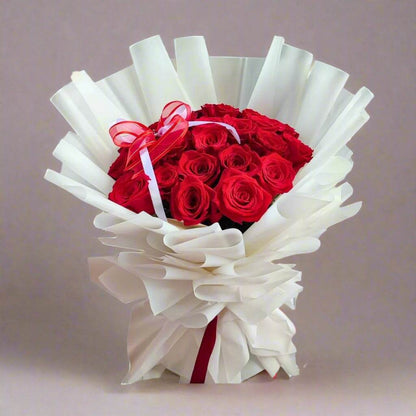 Bouquet of red roses wrapped in white paper with a red ribbon on a white background