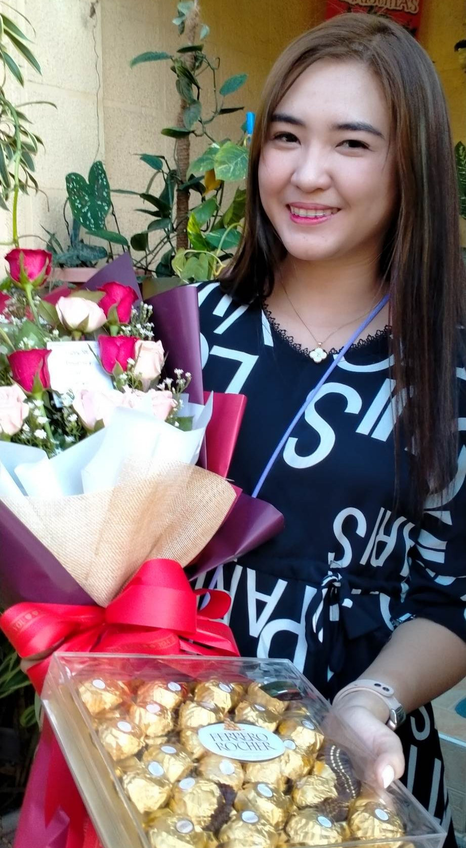 Woman holding a bouquet of flowers and a box of chocolates in an outdoor setting.