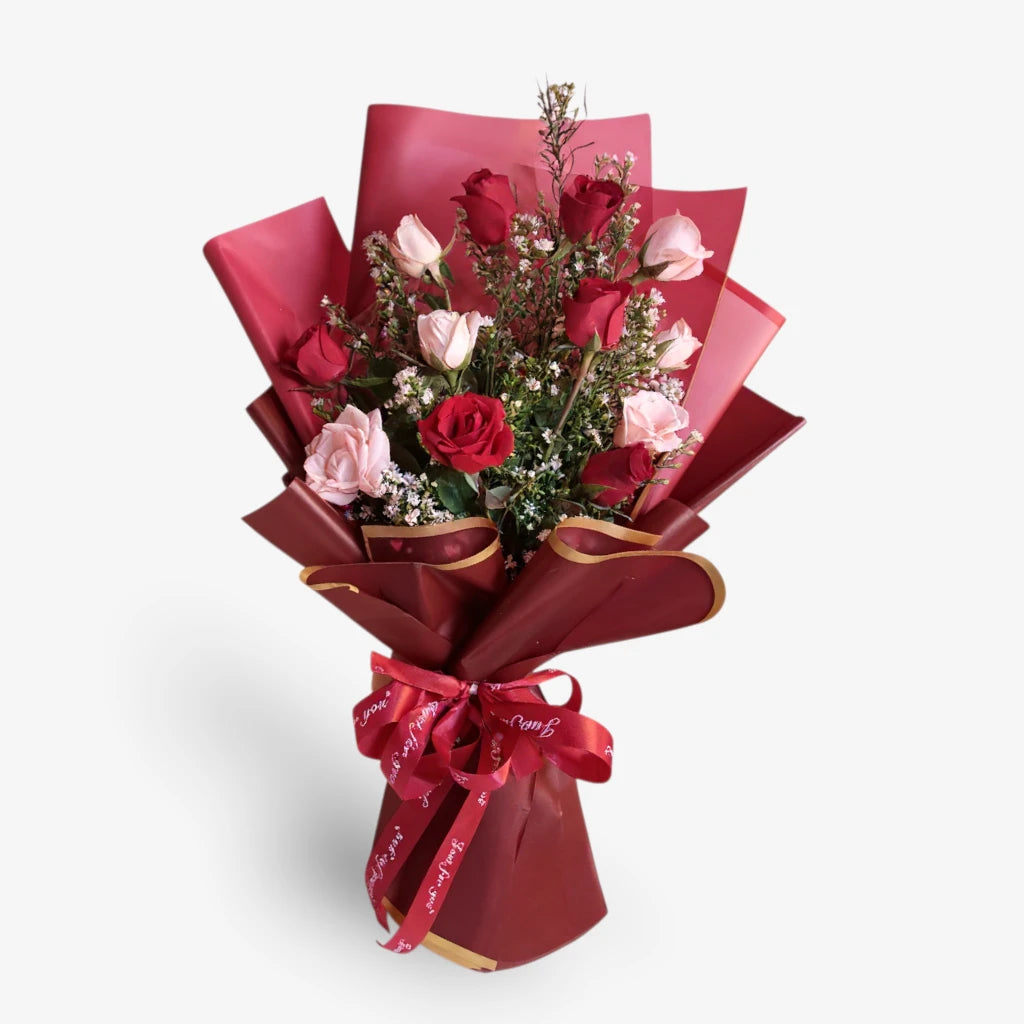 Bouquet of red and pink flowers wrapped in red paper with a bow on a white background