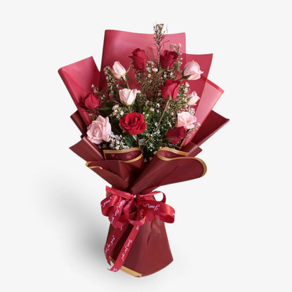 Bouquet of red and pink flowers wrapped in red paper with a bow on a white background