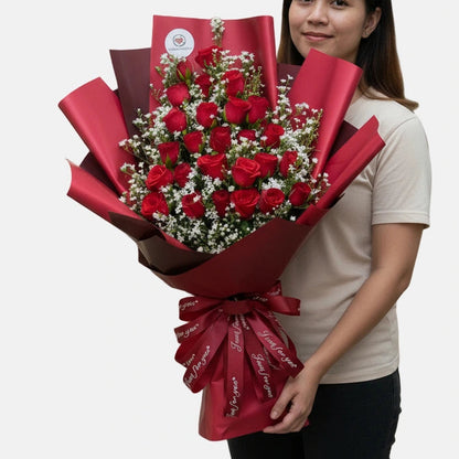 Person holding a large bouquet of red flowers wrapped in red paper against a white background