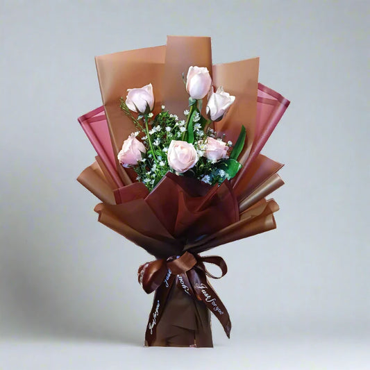 Bouquet of pink roses wrapped in brown paper with a ribbon on a light gray background