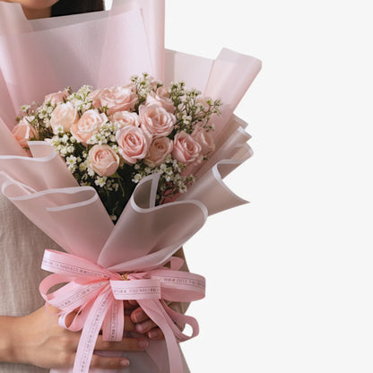 Bouquet of pink roses wrapped in white paper with a pink ribbon, held by a person.