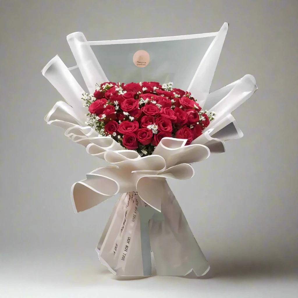 Bouquet of red roses wrapped in white paper with a decorative bow on a light gray background