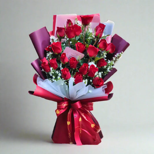 Bouquet of red roses wrapped in red and purple paper with a bow on a light gray background