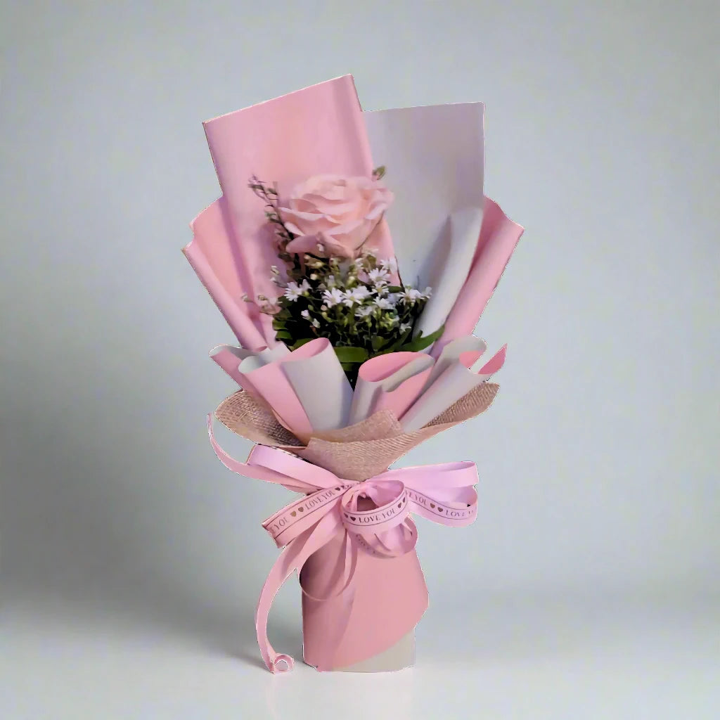 Bouquet of flowers wrapped in pink paper with a bow on a light gray background