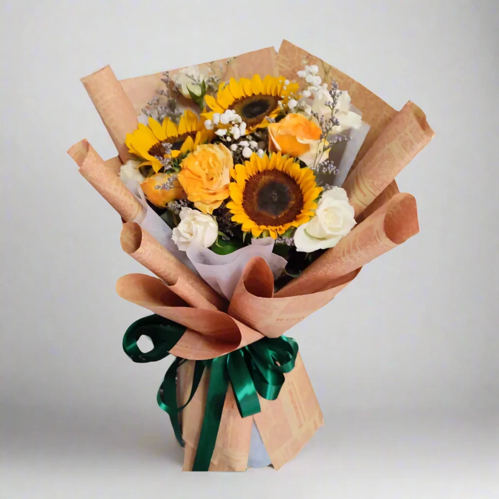Bouquet of sunflowers and other flowers wrapped in brown paper with a green ribbon on a light gray background