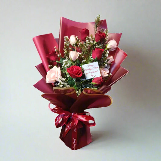 Bouquet of flowers wrapped in red paper with a card on a light gray background