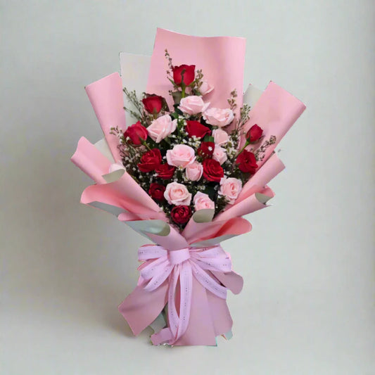 Bouquet of red and pink roses wrapped in pink paper with a bow on a light gray background