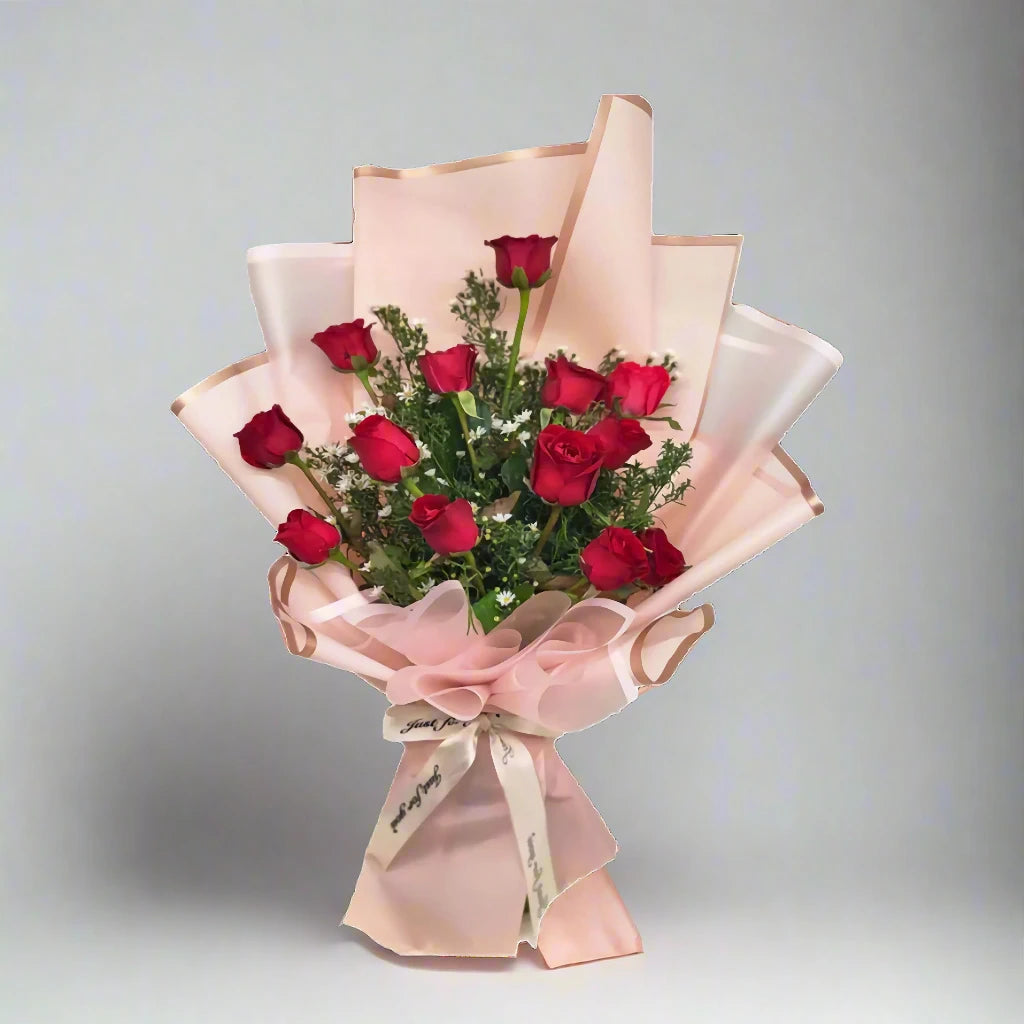 Bouquet of red roses wrapped in pink paper with a bow on a gray background