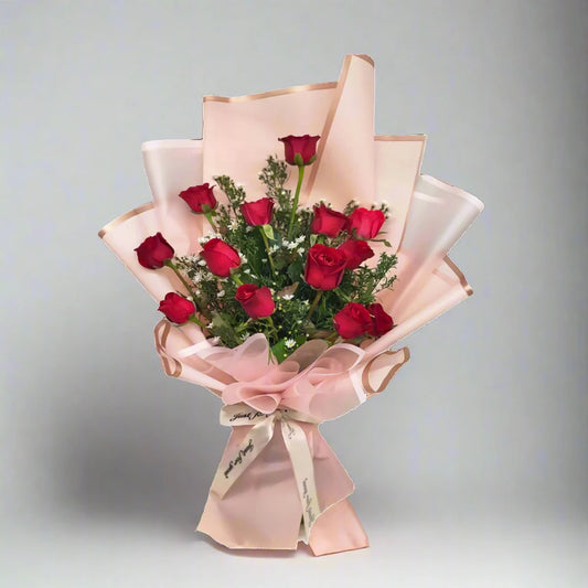 Bouquet of red roses wrapped in pink paper with a bow on a gray background