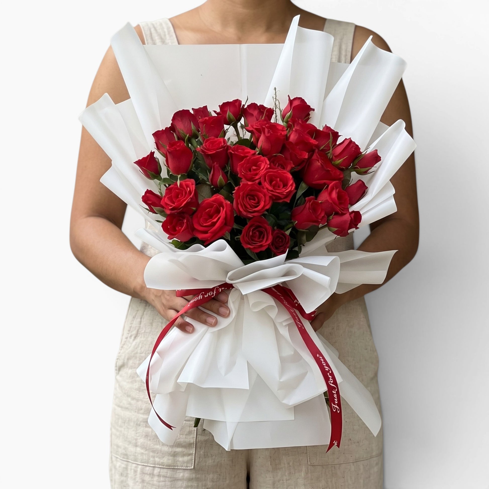 The Flowercart 36 Stalk of Love bouquet featuring red roses wrapped in white paper with a red ribbon held by a person
