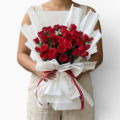 The Flowercart 36 Stalk of Love bouquet featuring red roses wrapped in white paper with a red ribbon held by a person