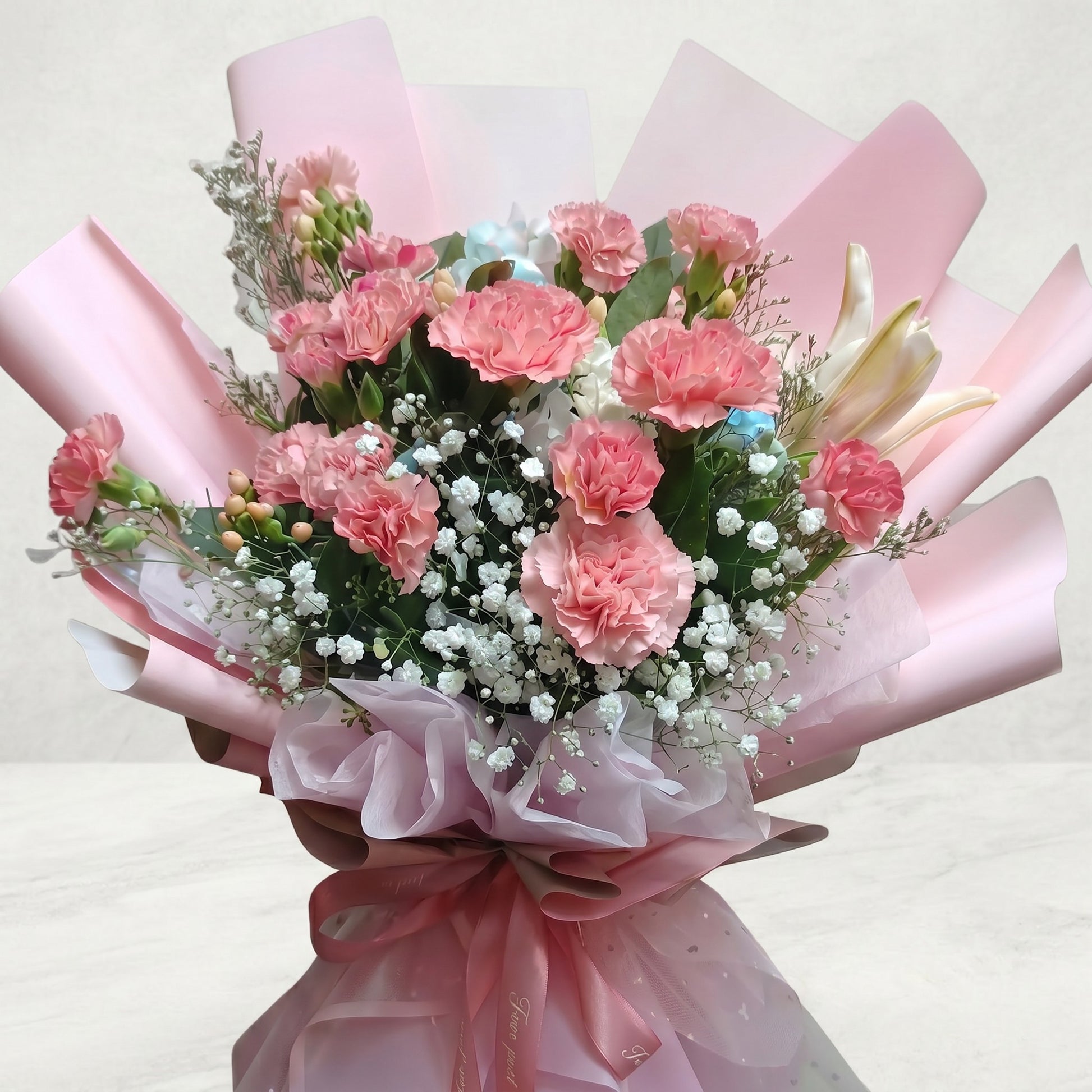 The Flowercart Berry Blush bouquet featuring pink carnations, baby's breath, and lilies in blush pink wrapping.