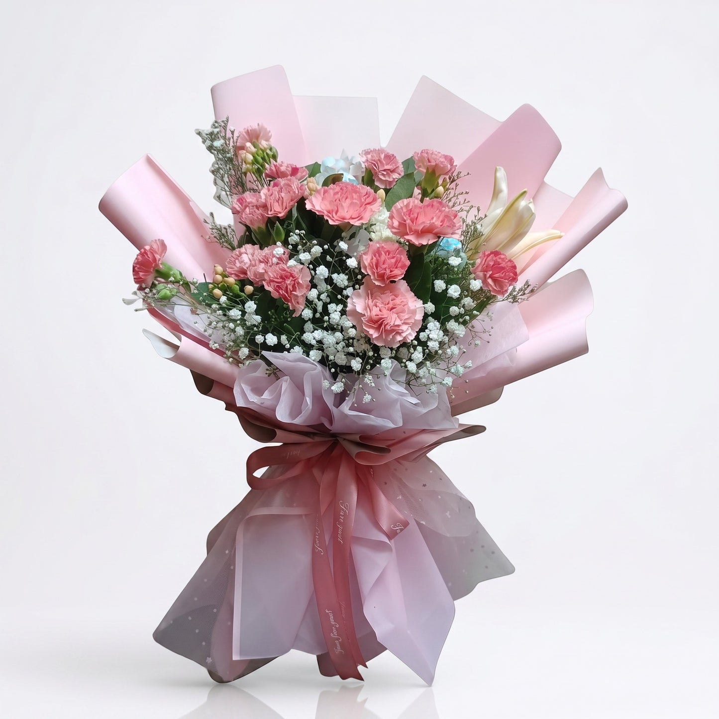 The Flowercart Berry Blush bouquet featuring pink carnations and baby's breath wrapped in blush pink paper with a ribbon.