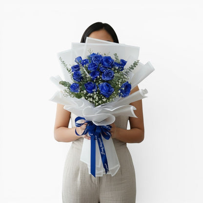 The Flowercart Sapphire Devotion bouquet featuring blue roses, baby's breath, and eucalyptus wrapped in white paper.