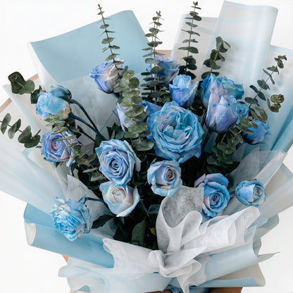 The Flowercart bouquet of 24 spray blue roses and eucalyptus wrapped in light blue paper for celebrations.