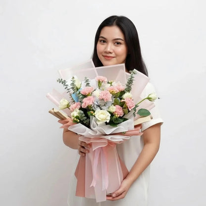 The Flowercart Carnation Carnival bouquet with pink carnations, white roses, blue hydrangeas, and eucalyptus held by a woman.