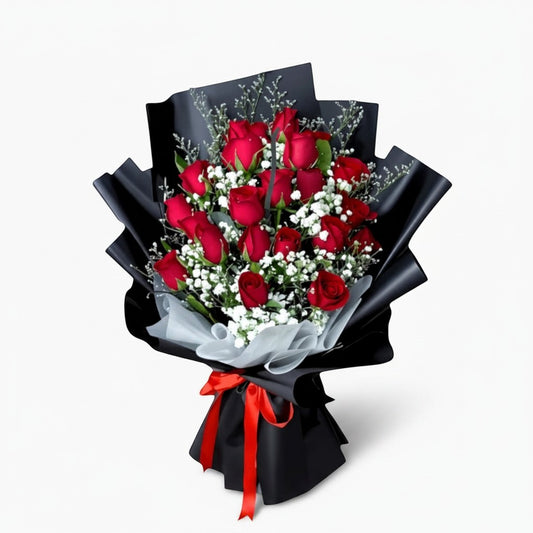 The Flowercart Luxe Noir bouquet featuring 24 red roses with white fillers wrapped in elegant black paper and red ribbon