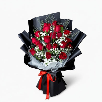 The Flowercart Luxe Noir bouquet featuring 24 red roses with white fillers wrapped in elegant black paper and red ribbon